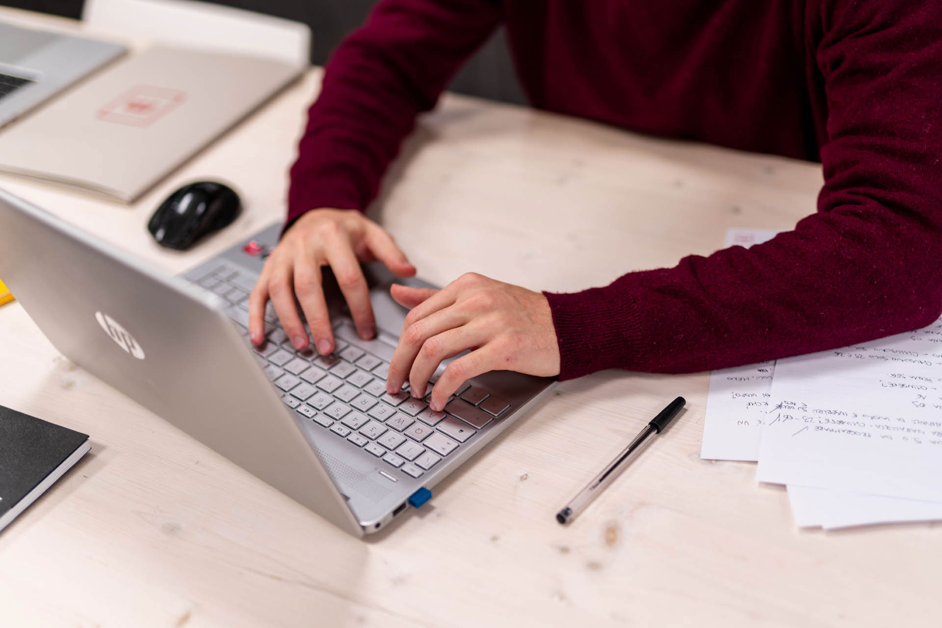 mani che digitano su una tastiera di un portatile. Sul tavolo sono presenti anche degli appunti su carta. Il tone of voice nasce proprio da qui